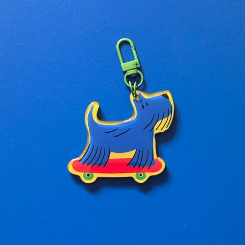 Dwa niebieskie breloki Piesek Jake na czerwonej deskorolce, z zielonym karabińczykiem, oraz dwie pasujące karty z napisem Jake.
