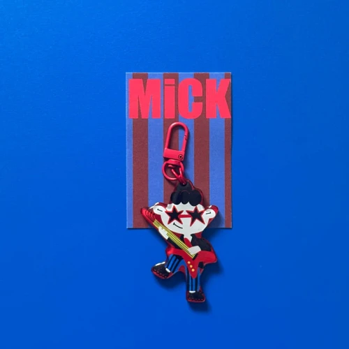 Designerski brelok Rockman Mick z czerwoną gitarą i gwiazdkami, z czerwonym karabińczykiem, na niebieskim tle.
