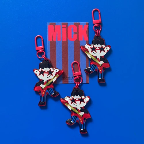 Designerski brelok Rockman Mick z czerwoną gitarą i gwiazdkami, z czerwonym karabińczykiem, na niebieskim tle.
